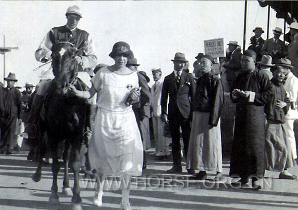 20世纪初天津赛马场的一个情景：这位女士是这匹马的主人，旁边一个华人正在纸上记录着.jpg